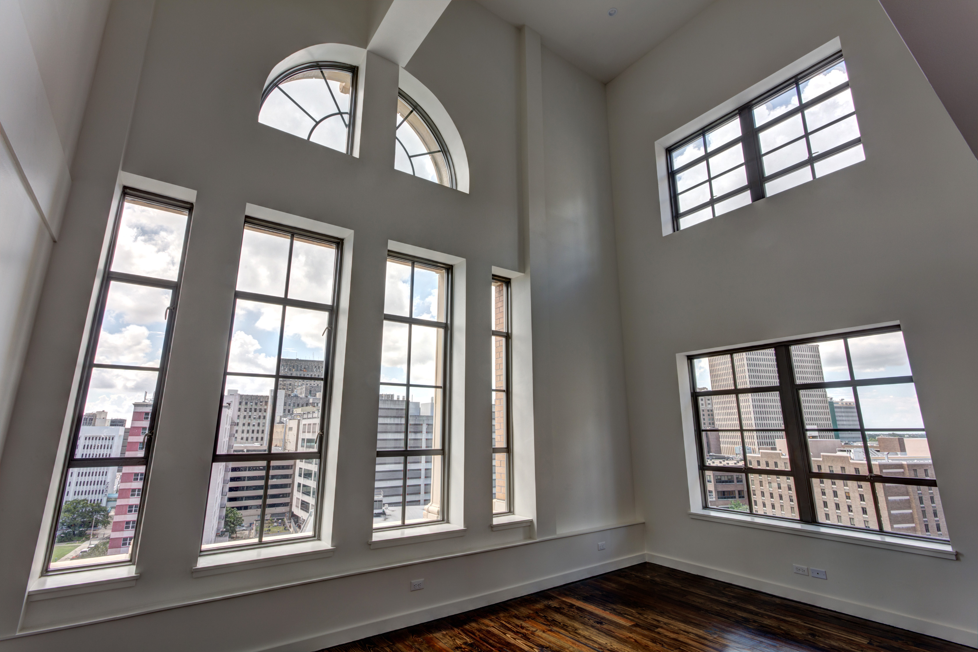 The inside of The Pythian, a 10-story high-rise in New Orleans. There are four tall, thin, steel windows under a semi-circle window on one wall, and two large steel horizontal windows on the other wall.