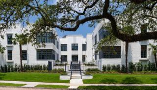 White brick building with large black windows and trees in background. 