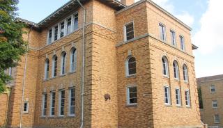 Tall beige brick building with windows and tree in background 